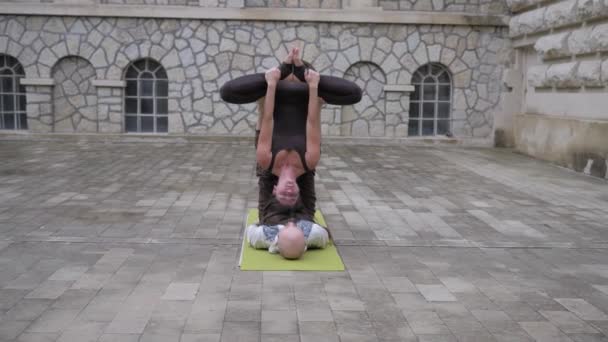Yoga acrobático. La mujer medita cabeza abajo, posición de loto al revés, haciendo ejercicios de acroyoga. Al revés, hombre. Al aire libre — Vídeos de Stock