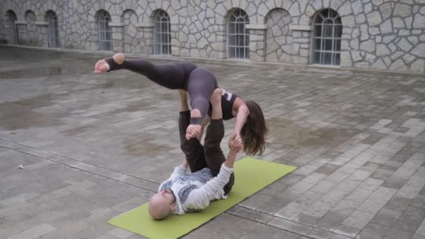 Fit couple sportif pratiquant l'acro yoga avec partenaire ensemble sur le tapis, jeune homme tenant les femmes en équilibre sur ses pieds, faire de l'exercice acrobatique à l'extérieur — Video