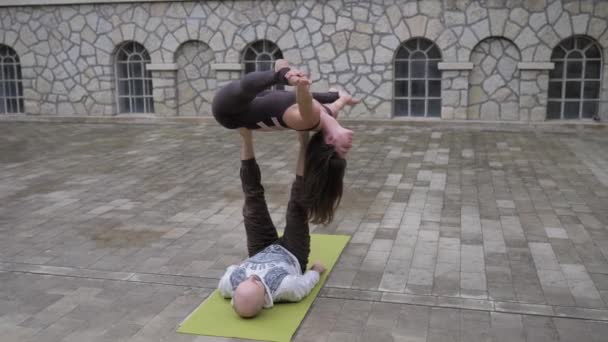 Fit sportief paar oefenen acro yoga met partner samen op de mat buiten. Een paar acrobatische oefeningen. Vrouwelijke acrobaat balanceert op de benen van haar mannelijke partner — Stockvideo