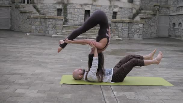 Yoga acrobático. Una mujer se equilibra en el pie de mano de un hombre mientras hace ejercicios de acroyoga. En el contexto de la antigua ciudad — Vídeo de stock