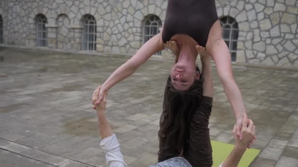 Akrobatik yoga. Kadın, erkek kollarına yaslanarak akroyoga egzersizleri yaparken amuda kalkıyor. Açık havada. — Stok video