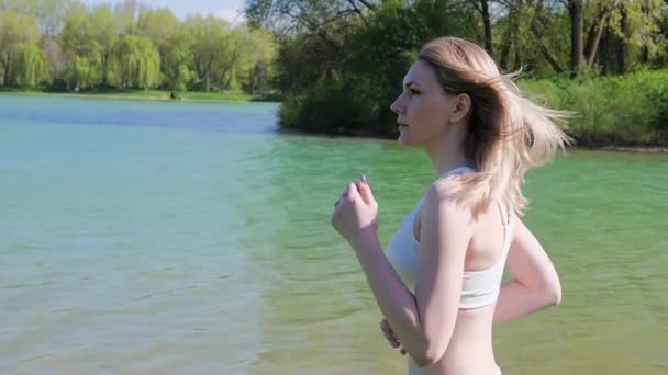 公園の湖のそばをジョギングしている若い運動女子の肖像画です。スローモーション — ストック動画