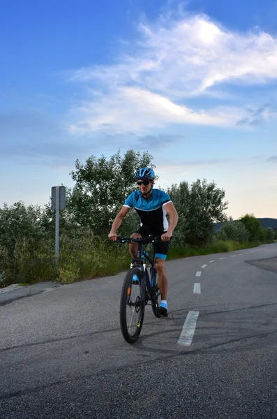 Ciclista indo de bicicleta de montanha ao longo de uma estrada solitária — Fotografia de Stock