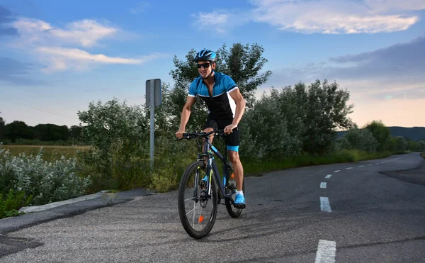 Ciclista indo de bicicleta de montanha ao longo de uma estrada solitária — Fotografia de Stock