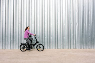 Şehrin sokaklarında elektrikli bisiklet süren 40 yaşında bir kadın (Elektrikli Hareket kavramı))