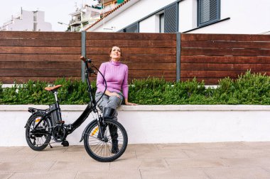 Şehrin sokaklarında elektrikli bisiklet süren 40 yaşında bir kadın (Elektrikli Hareket kavramı))