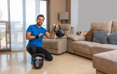 Latin bir adam evde bir çift kettlebell ile haç egzersizi yapıyor..