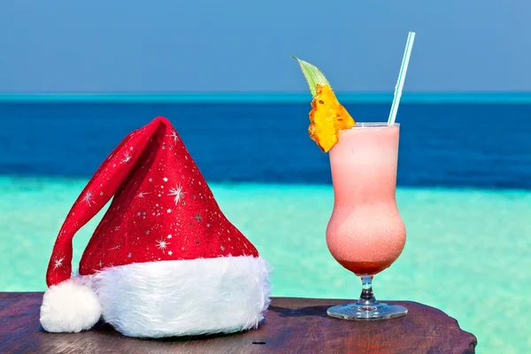 Бокал напитка на пляжном столе с шапкой Санты — стоковое фото