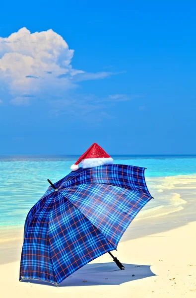 Blue Umbrella Is On A Beach With Santa Hat — Stock Photo, Image