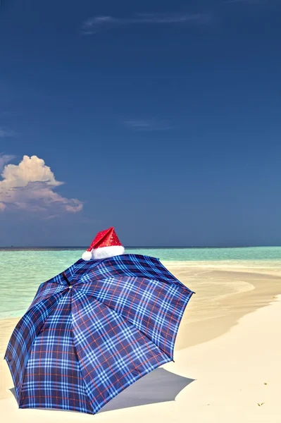 Paraguas azul está en una playa con sombrero de Santa — Foto de Stock