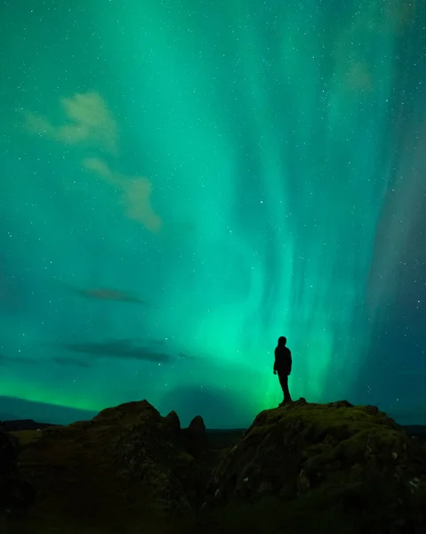 An adventure solo traveler posing with the beautiful northern lights also known as aurora borealis in the background. A breathtaking nature of Iceland as nordic country