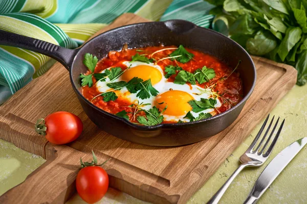 Delicioso shakshuka de Oriente Medio huevos fritos, cebolla, pimiento, tomates, chile y especias en estofado de hierro fundido con toalla de cocina sobre fondo viejo, receta auténtica — Foto de Stock