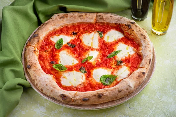 Italiaanse pizza met tomaat belegd met gesmolten gouden kaas, kruiden en basilicum op lichte tafel — Stockfoto