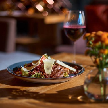 Kızarmış dana eti, domates, patlıcan ve restorandaki masada bir bardak kırmızı şarap.