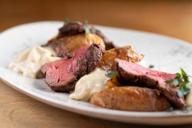 Bakır bir çarşaf üzerinde yeşil, baharat ve sebzelerden oluşan siyah bir tabakta mignon filetosu. Kapat..