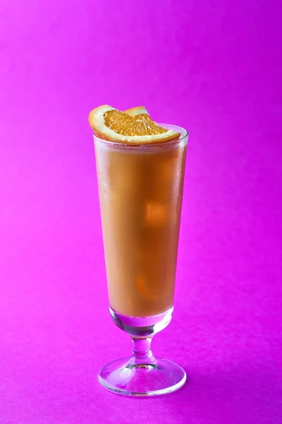 Orange and coffee cocktail topping sliced orange on a purple background.