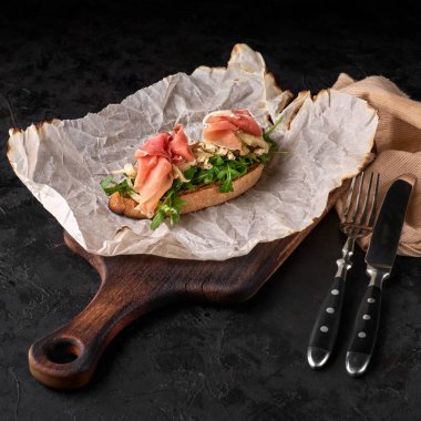 Parma jambonlu bruschetta, yumuşak peynirli ve olgun armut tostlu, ahşap kesme tahtasında servis edilen siyah arka planda..