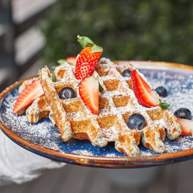 Traditional Belgian dessert in the hands on the summer terrace, breakfast time- waffle with strawberry and cream.