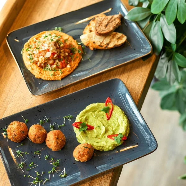 Hummus de grão de bico e guacamole e prato de falafel em chapa azul em uma mesa de madeira. — Fotografia de Stock