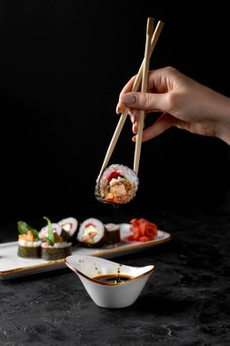 Siyah desenli bir arka planda yemek çubuğuyla Futo Maki 'yi tutuyor. Suşi menüsü. Japon yemeği..