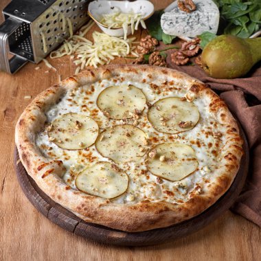 Pizza tahtasında taze roka ile süslenmiş armut ve küflü peynirli pizza.