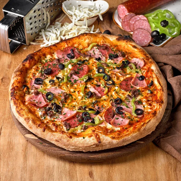 Traditional italian Pizza with salami, mozzarella, ham and bacon on wooden background. Fast food lunch for picnic company, photo for the menu. Italian cuisine.