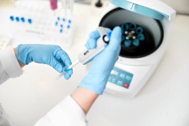 Araştırmacı, laboratuardaki bir santrifüje pipet ve analiz tüpü numuneleri kullanıyor. Kadın araştırmacı test tüplerini özel makineye yerleştiriyor..