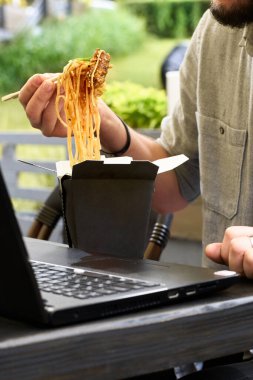 Parkta öğle yemeği vakti. Wok siyah yemek kabında kutuda, maket. Çubuklu baharatlı erişte tutuyorum. Fast food teslimat servisi. Çin yemeği siparişi.