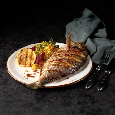 Bulgur ve biberli Dorado, limon ve bal soslu. Baharatlı ve otlu kavrulmuş deniz ürünleri. Menü için fotoğraf. Siyah beton arkaplan.