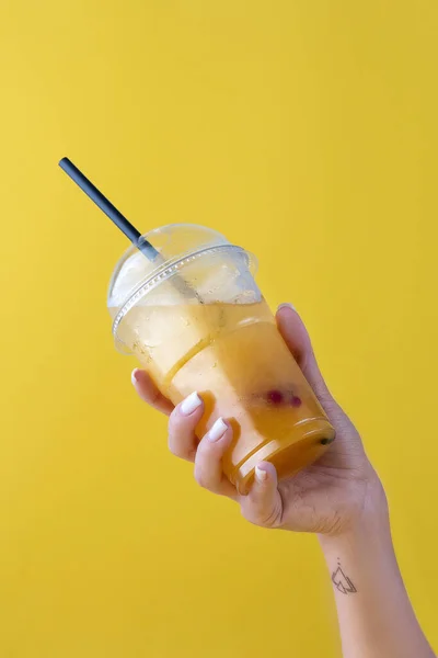 Summer Drink Fresh Lemonade with orange in the plastic cup on yellow background. female hand holding a glass. Mockup for your advertisement. — Stock Photo, Image