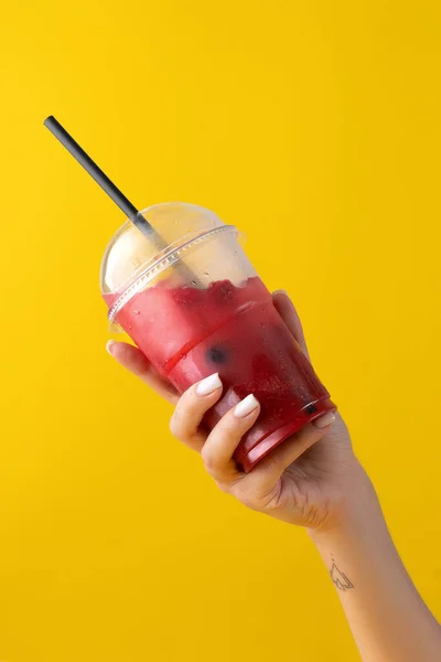 Summer Drink Fresh Lemonade with strawberry in the plastic cup on yellow background. female hand holding a glass. Mockup for your advertisement. — Stock Photo, Image