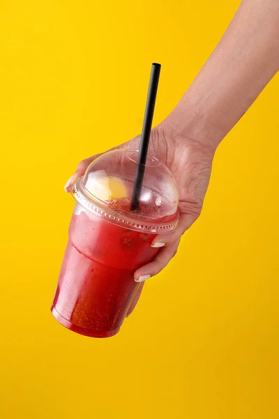 夏天喝新鲜的柠檬水，在黄色背景的塑料杯里放草莓。手里拿着杯子的女人。为你的广告配音. — 图库照片