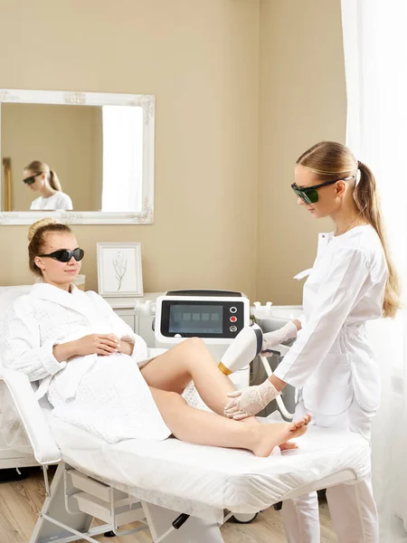 Cosmetologia. Giovane donna al salone Spa che riceve la procedura di depilazione laser. Estetista utilizzando apparati moderni per le procedure termali. Cura della pelle e bellezza. — Foto Stock