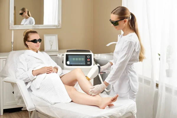 Cosmetologia. Giovane donna al salone Spa che riceve la procedura di depilazione laser. Estetista utilizzando apparati moderni per le procedure termali. Cura della pelle e bellezza. — Foto Stock