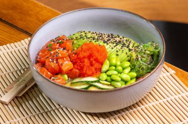 Somon, avokado, ahşap arka planda edamame fasulyesi. Modaya uygun sağlıklı deniz ürünleri tabağı. Restoran masasında..