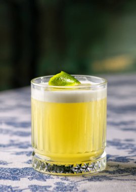 Pisco kokteyli - limonlu viski, yumurta beyazı, bardakta şeker şurubu, arka planda duvar. Kokteyl masanın üstünde. Metin için boşluk.