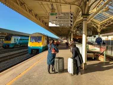 Cardiff, Wales - Şubat 2018: Cardiff Merkez Tren İstasyonu 'ndaki bir platformda bavullu iki yolcu ve arka planda bir tren var.