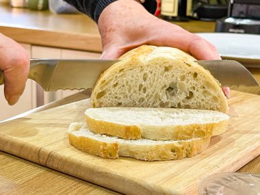 Bir somun ekmek, tahta bir ekmek tahtasında bıçakla dilimleniyor.