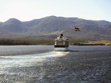 Ketchikan, Alaska, ABD - Ağustos 2012: Turistik bir geziden dönen bir deniz uçağı, kentten ayrılırken Milenyum yolcu gemisinin yanından geçiyor