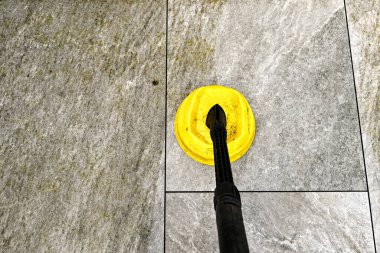 Bahçe avlusundaki porselen levhaları temizlemek için basınç makinesinde kullanılan eklenti, temiz ve kirli levhalar arasındaki farkı gösteriyor..  