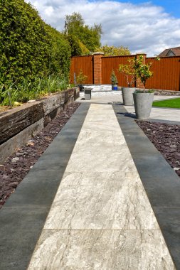 Açık ve koyu gri porselen döşeme levhalarıyla döşenmiş bir arka bahçenin yolu. Kimse yok..