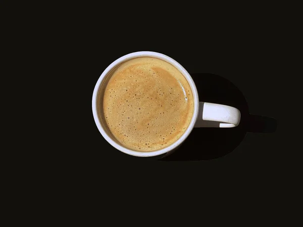 Overhead view of a cup of fresh frothy coffee on a plain dark table top. No people.  Copy space.