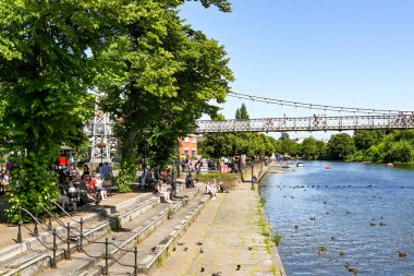 Chester, Cheshire, İngiltere - Temmuz 2021: Chester 'ın merkezinden geçen Dee Nehri' nin kıyısında oturan insanlar