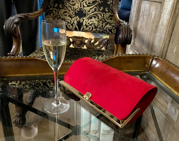 Clutch handbag and a glass of champagne on a table at a hotel. No people.