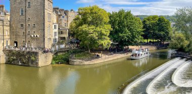 Bath, İngiltere - Ağustos 2021: Bath 'ın merkezindeki Pultney Köprüsü' nde panoramik manzara. Arka planda ziyaretçileri Avon Nehri 'ne götüren bir tur teknesi var..