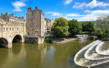 Bath, İngiltere - Ağustos 2021: Bath 'ın merkezindeki Pultney Köprüsü' nde at nalı şekilli Weir. Arka planda ziyaretçileri Avon Nehri 'ne götüren bir tur teknesi var..