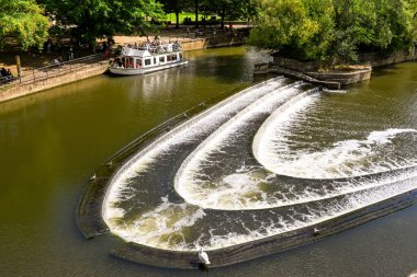 Bath, İngiltere - Ağustos 2021: Bath 'ın merkezindeki Pultney Köprüsü' nde at nalı şekilli Weir. Arka planda ziyaretçileri Avon Nehri 'ne götüren bir tur teknesi var..