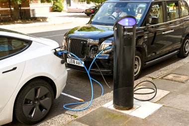 Londra, İngiltere - Ağustos 2021: Araba ve bir Londra taksisi bir elektrik şarj istasyonuna takıldı