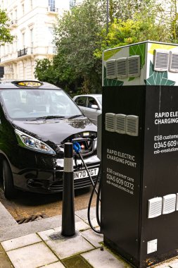 Londra, İngiltere - Ağustos 2021: Londra taksisi bir şehir caddesinde elektrik tesisatına tamamen bağlı..