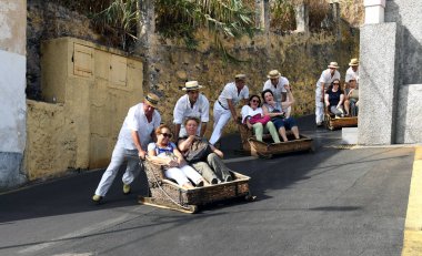 Madeira, Portekiz - Eylül 2017: Geleneksel giysiler içindeki katılımcılar tarafından kontrol edilen Funchal kentinin yukarısındaki dik bir tepeden sepetle kayan ziyaretçiler